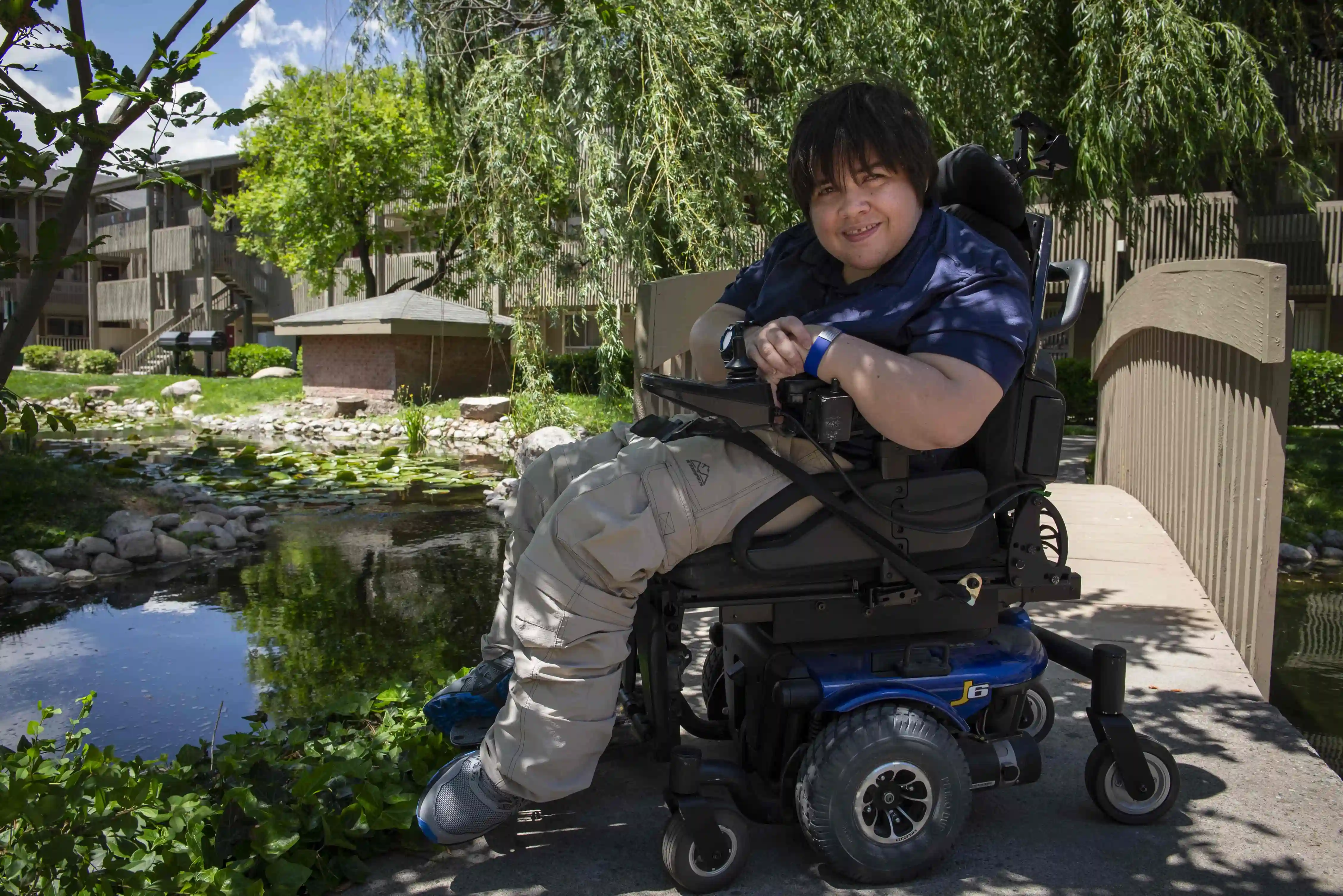 A young man in a wheelchair in a park near an apartment complex