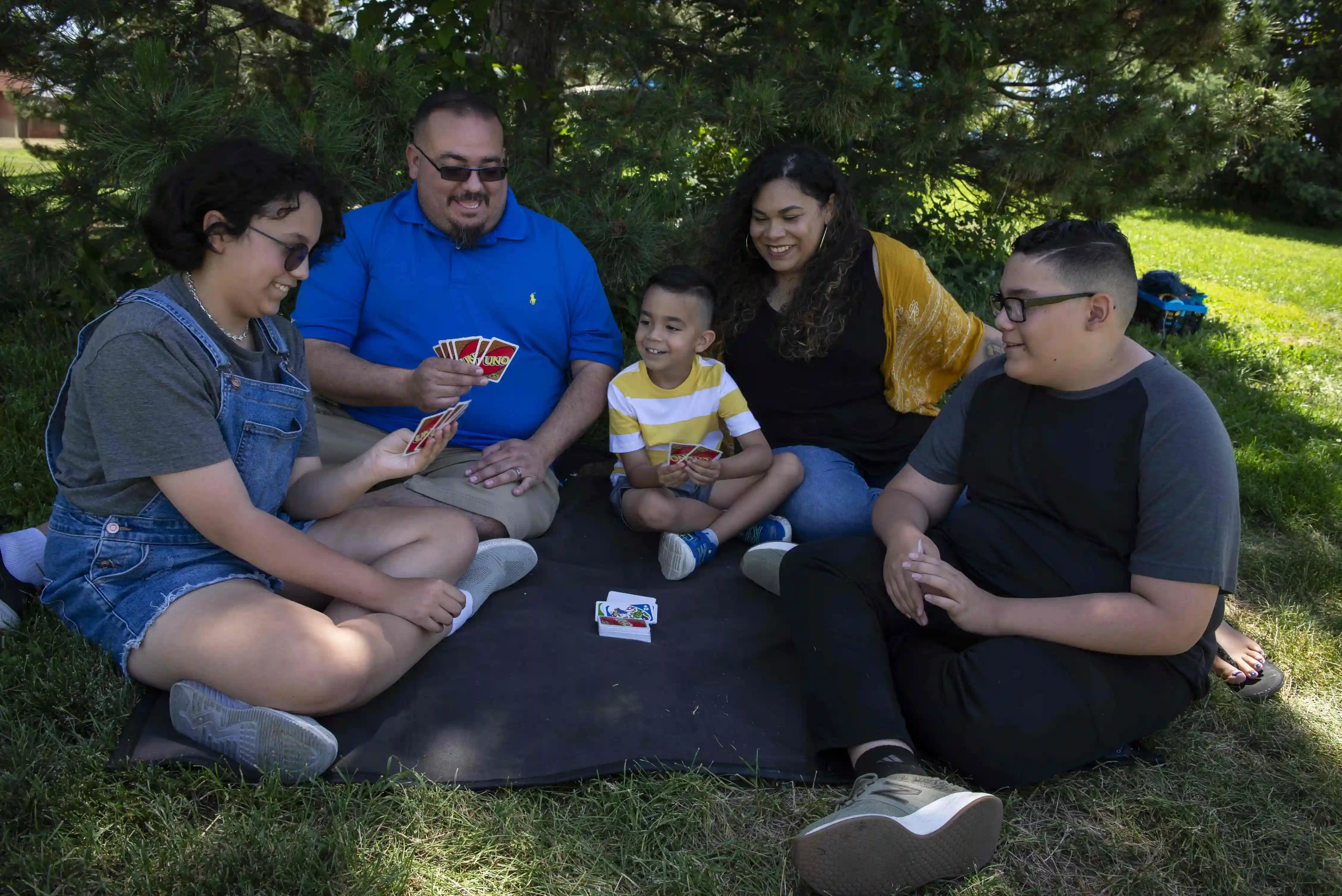 A family of five relaxing under a tree enjoying a card game