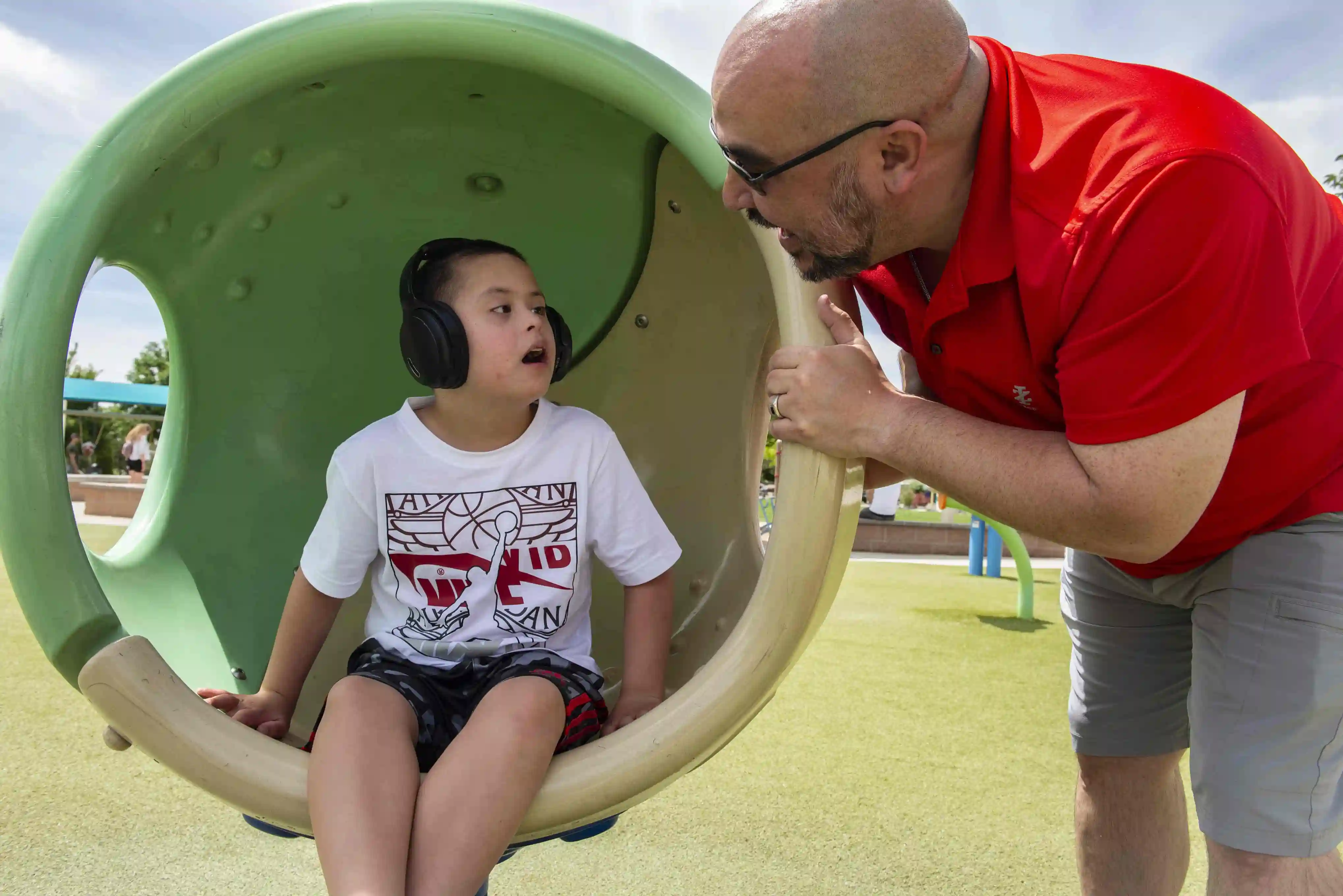 A young boy sitting on playground equipment with a caregiver