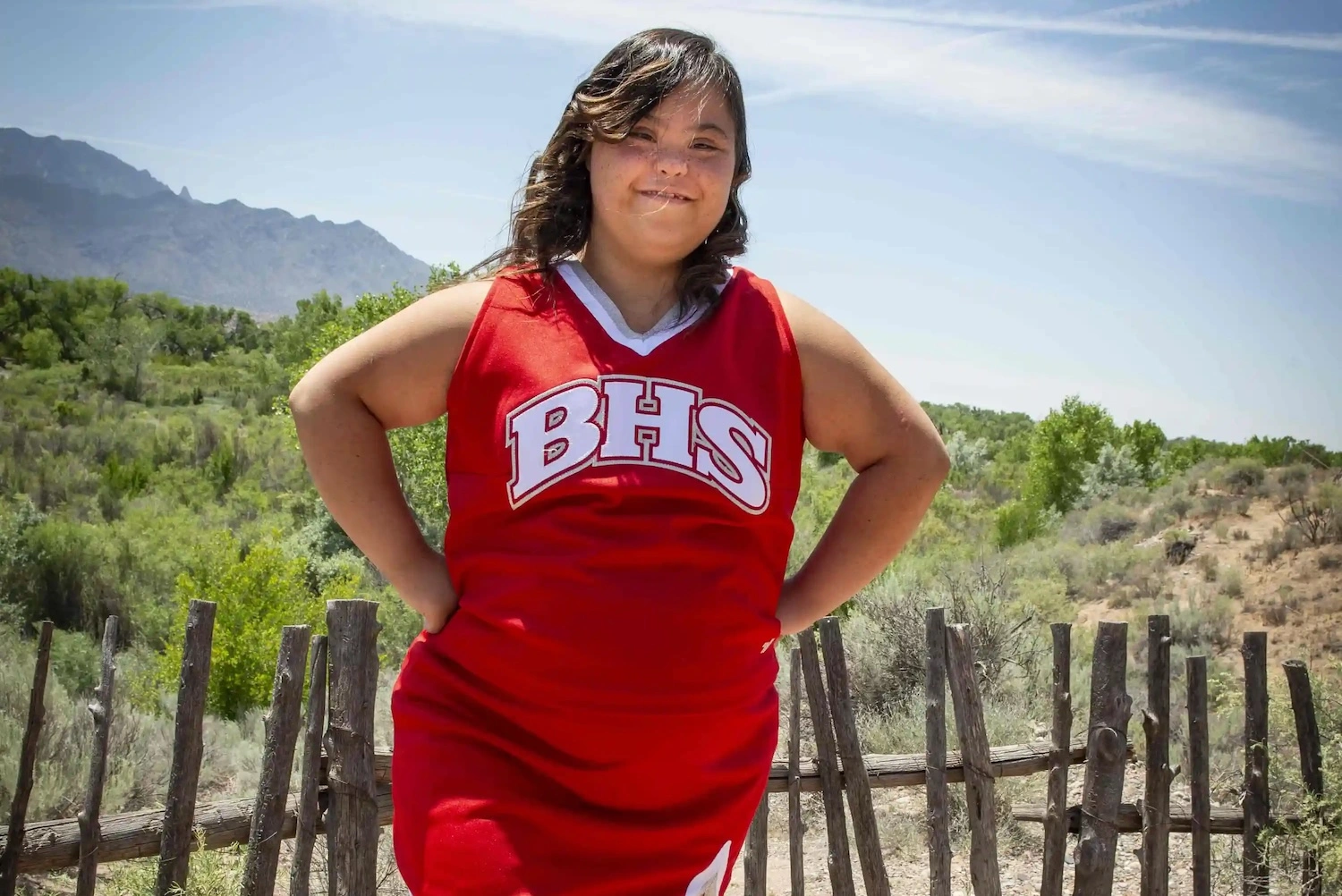 A young lady poses in her cheerleading outfit in front of a mountain landscape